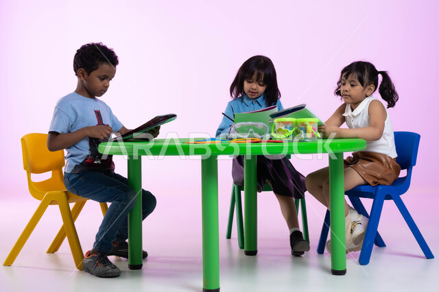 الجلسات والحصص التعليمية في الروضات السعودية، بورتريه لأطفال عرب خليجيين سعوديين يرتدون الزي الكاجوال يقومون بتلوين الرسومات بايماءات الاندماج، القيام بالمهارات و الأنشطة المختلفة لتنمية القدرات العقلية والذهنية، خلفية وردية.