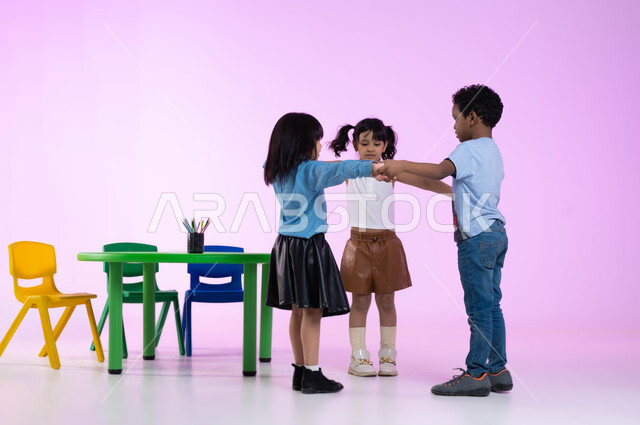 مفهوم دمج المتعة بالفائدة، العاب تعليمية ترفيهية، قضاء أوقات ممتعة ومفيدة في الروضة، تعليم وإبداع وتنمية مهارات في رياض الأطفال، بورتريه لأطفال عرب خليجيين سعوديين يرتدون الزي الكاجوال يلعبون ويمرحون، إيماءات تدل على الفرح والسعادة، صورة لكامل الجسم، خلفية وردية