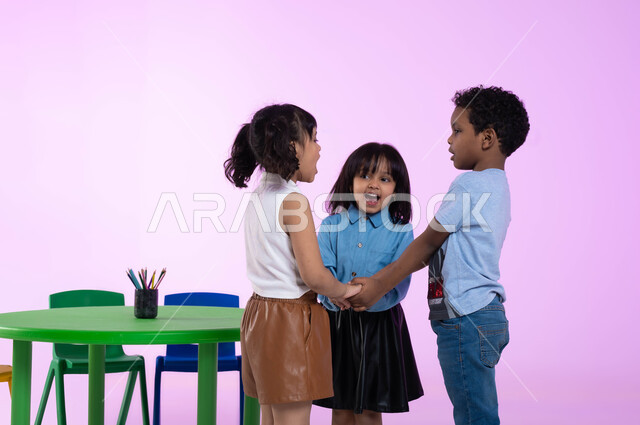 Spending fun and useful times in kindergarten, the concept of combining fun with benefit, educational entertaining games, education, creativity and skill development in kindergarten, a portrait of Saudi Gulf Arab children wearing casual clothes playing and having fun, gestures indicating joy and happiness, a pink background