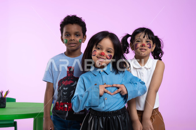 Heart-shaped hand gestures, feeling of love and admiration, drawing on children’s faces with healthy colors, spending fun and useful times in the kindergarten, close-up portrait of Saudi Gulf Arab children wearing casual clothes looking at the camera with expressions indicating happiness, pink background