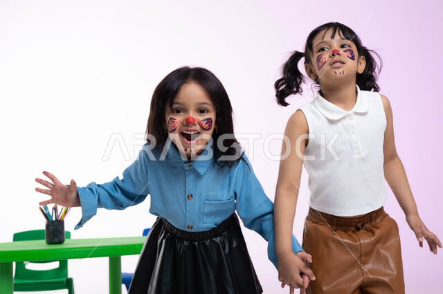 إيماءات تدل على الفرح والسعادة، التظاهر والتمثيل بالحيوانات المفترسة، قضاء أوقات ممتعة بالقيام بأنشطة ترفيهية في الروضة، بورتريه لطفلتين عربيتين خليجيتين سعوديتين ترتديان الزي الكاجوال تلعبان وتمرحان، الرسم بألوان صحية على وجوه الأطفال، خلفية وردية