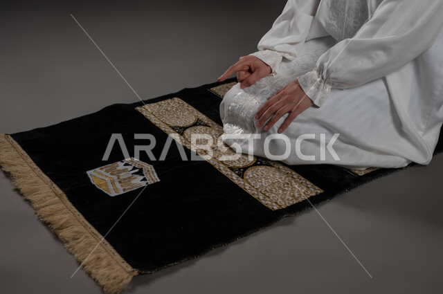 رفع اصبع السبابة للأعلى، مفهوم أركان الاسلام والأيمان، الالتزام بأداء الفروض على وقتها, التقرب الى الله بالإجتهاد في العبادة والحفاظ على الصلوات، بورتريه مقرب لإمرأة عربية سعودية خليجية تجلس على سجادة الصلاة تقوم بالتشهد، خلفية سوداء
