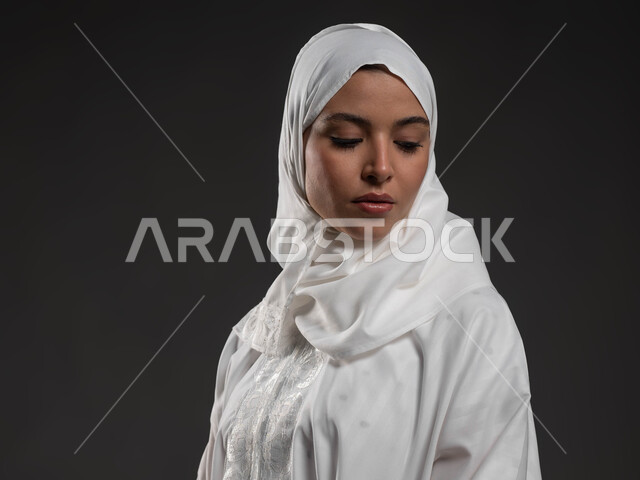 مفهوم أركان الاسلام، التقرب الى الله بالإجتهاد في العبادة والحفاظ على الصلوات، بورتريه مقرب لإمرأة عربية سعودية خليجية ترتدي الحجاب والعباءة البيضاء تقوم بالتسليم في الركعة الاخيرة من الصلاة، الالتزام بأداء الفروض على وقتها, خلفية سوداء