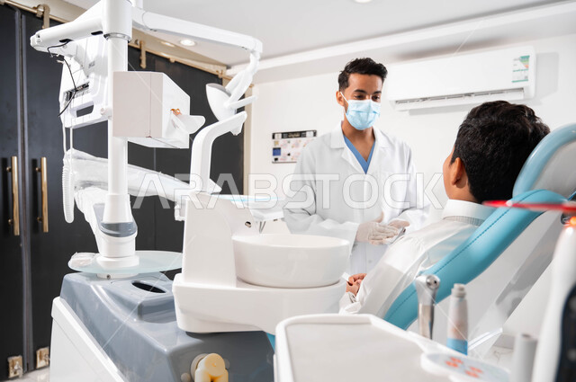 الإرشادات والتعليمات الطبية، طبيب أسنان يتحدث مع مريضه بإيماءات الاطمئنان، ولد عربي خليجي سعودي يجلس في عيادة سنية يتلقى النصائح، العناية والاهتمام بالصحة الفموية، معالجة الأسنان من النخور والتسوس، الزيارة الدورية للعيادات الصحية
