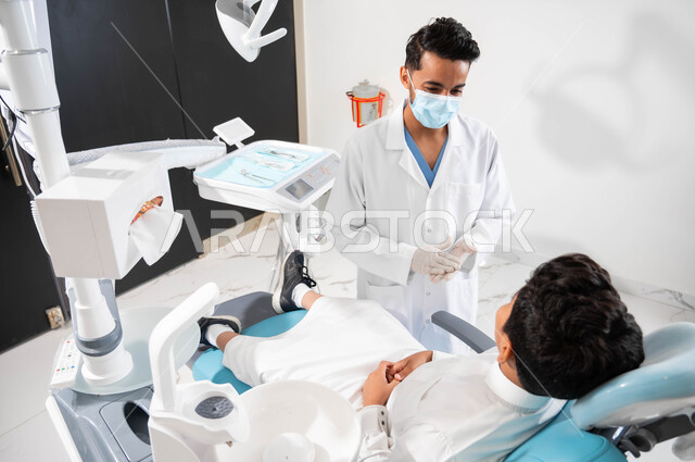 الإرشادات والتعليمات الطبية، طبيب أسنان يتحدث مع مريضه بإيماءات الاطمئنان، ولد عربي خليجي سعودي يجلس في عيادة سنية يتلقى النصائح، العناية والاهتمام بالصحة الفموية، معالجة الأسنان من النخور والتسوس، الزيارة الدورية للعيادات الصحية