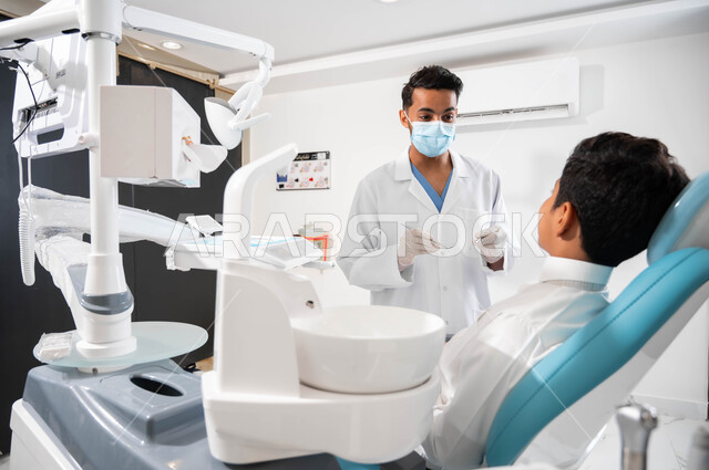 Medical advice and instructions, a dentist talking to his patient with reassuring gestures, a Saudi Gulf Arab boy sitting in a dental clinic receiving advice, care and attention to oral health, treating teeth for caries and decay, periodic visits to health clinics