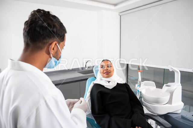 الإرشادات والتعليمات الطبية، أطبيب أسنان عربي خليجي سعودي يتناقش مع مريضته، إمرأة عربية خليجية سعودية محجبة تجلس في عيادة سنية تنظر بإيماءات السرورتتلقى النصائح، العناية والاهتمام بالصحة الفموية