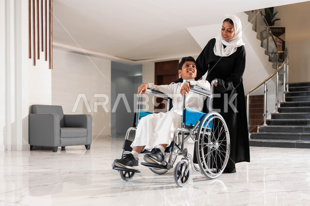 الاهتمام بالجانب النفسي لأصحاب الهمم, رعاية الأبناء والاعتناء بذوي الاحتياجات الخاصة, أم عربية سعودية خليجية محجبة تقوم بمساعدة ابنها في التنقل داخل المنزل, ولد سعودي مقعد يجلس على كرسي متحرك ,تأمين معدات تساعد على الحركة, شعور المعاقين بالتقدير في السعوديه