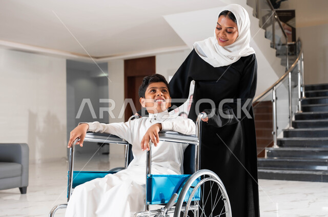 رعاية الأبناء والاعتناء بذوي الاحتياجات الخاصة, أم عربية سعودية خليجية محجبة تقوم بمساعدة ابنها في التنقل, ولد سعودي مقعد يجلس على كرسي متحرك ,تأمين معدات تساعد على الحركة, الاهتمام بالجانب النفسي لأصحاب الهمم, شعور المعاقين بالإنتماء والتقدير في السعوديه