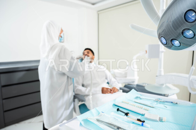 زيارة العيادات الصحية واتخاذ الإجراءات اللازمة، صورة مقربة للمعدات والأدوات اللازمة لجراحة الفم, داخل المراكز الطبية, طبيبة عربية خليجية سعودية تقوم بفحص أسنان المريض و تشخيص المرض، إجراء الفحوصات الدورية للعناية بالصحة الفموية, معالجة التسوس وتركيب الحشوات