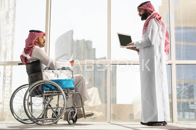 مفهوم التركيز والدقة في الإنجاز, النجاح في تحقيق أهداف واستراتيجيات الشركة, تأمين اجهزة ومعدات تساعد بالحركة والتنقل صورة من الجانب لموظفان عربيان خليجيان سعوديان يرتديان الزي التقليدي السعودي يقومان بالحوارات والنقاشات في الشركة الراقية بجانب النافذة الزجاجية