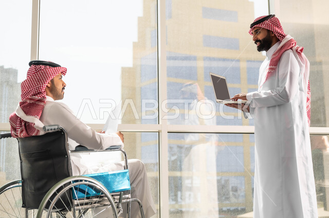 النجاح في تحقيق أهداف واستراتيجيات الشركة, مفهوم التركيز والدقة في الإنجاز, صورة من الجانب لموظفان عربيان خليجيان سعوديان يرتديان الزي التقليدي السعودي يقومان بالحوارات والنقاشات في الشركة الراقية بجانب النافذة الزجاجية, تأمين اجهزة ومعدات تساعد بالحركة والتنقل