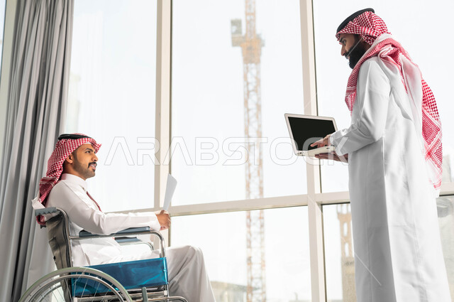 النجاح في تحقيق أهداف واستراتيجيات الشركة, تأمين اجهزة ومعدات تساعد بالحركة والتنقل صورة من الجانب لموظفان عربيان خليجيان سعوديان يرتديان الزي التقليدي السعودي يقومان بالحوارات والنقاشات في الشركة الراقية بجانب النافذة الزجاجية, مفهوم التركيز والدقة في الإنجاز