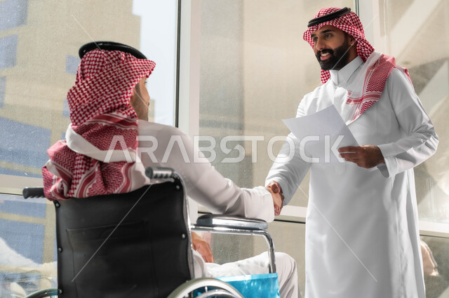 التعرف على الزملاء الجدد، عقد الاتفاقات والصفقات التجارية، اتاحة المجال امام ذوي الهمم للدخول الى مجال العمل، الترحيب والاستقبال وبناء العلاقات الاجتماعية، صورة مقربة لرجلين عربيين سعوديين خليجين  يرتديان الشماغ والثوب السعودي التقليدي يقومان بمصافحة بعضهما