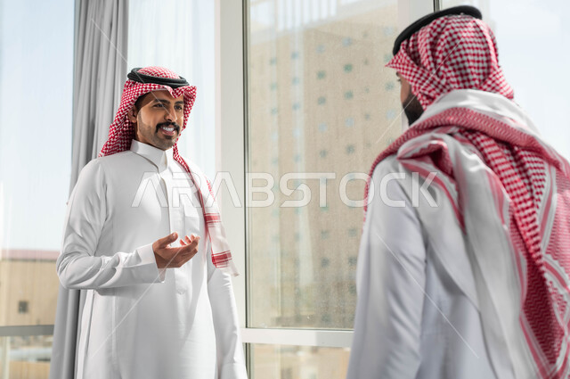 وظائف ومهام ادارية مكتبية، الاستعداد والتجهز لحضور الاجتماع، جودة الحياة في الشركات السعودية، صورة مقربة لرجلين عربيين خليجيين سعوديين يرتديان الشماغ والثوب التقليدي يقومان بالدردشة والتحدث داخل مقر الشركة، تبادل الخبرات بين الفريق لتحقيق الأهداف وتطوير الخطط