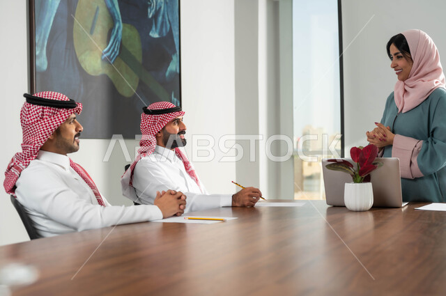 The concept of equality between women and men, a group of employees in the meeting room who engage in dialogue and exchange experiences within the company’s headquarters, lifestyle in Saudi companies, office administrative jobs, using the laptop to achieve goals and develop plans, cooperation and love among members of the same team.