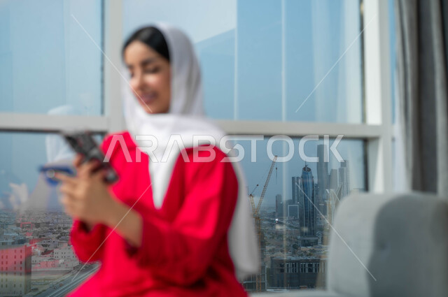 Expressions of pleasure using modern technologies and means, purchasing and paying through mobile programs and applications, the ability to pay bills via credit card, a smiling Saudi Arabian Gulf woman wearing the hijab holding a mobile phone and a bank credit card in her hand, the style and quality of life in the Kingdom.