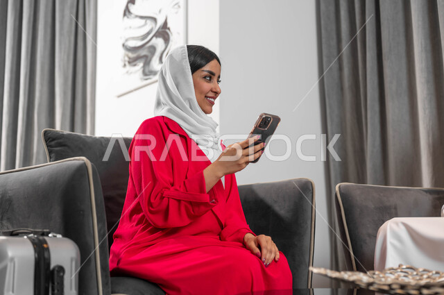 الجلوس في الفنادق الراقية، السفر والتنقل لتبادل الخبرات بين الشركات، جودة الحياة في السعودية، تحقيق الأهداف وتطوير الخطط، امرأة عربية خليجية سعودية ترتدي العباءة والحجاب تجلس في لوبي فندق تقوم باستخدام الهاتف الجوال والتحدث مع شخص ما