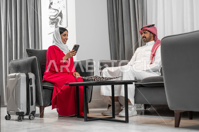 السفر والتنقل لتبادل الخبرات بين الشركات، عقد اجتماعات عمل في الفنادق الراقية، جودة الحياة في الشركات السعودية، رجل وسيدة عربيان خليجيان سعوديان يقومان بالدردشة والتحدث في لوبي الفندق، تحقيق الأهداف وتطوير الخطط، امرأة سعودية ترتدي العباءة والحجاب تستخدم الجوال