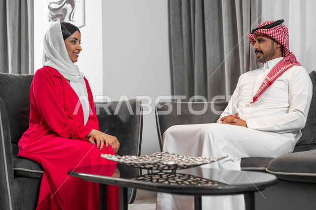 الإنصات والاستماع باحترام للحديث بين الزوجين، جلسات عائلية سعيدة، زوجان عربيان خليجيان سعوديان يجلسان في غرفة المعيشة يقومان بتبادل الأحاديث والحوارات بإيماءات المودة والتفاهم، مفهوم الألفة والمحبة بين الأزواج