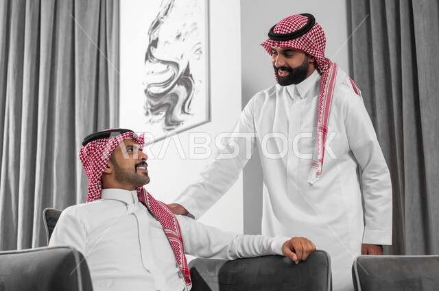 إلقاء التحية والسلام بإيماءات البشاشة والسرور، عقد اجتماعات عمل في الفنادق الراقية لتبادل الخبرات بين الفريق، تحقيق الأهداف وتطوير الخطط، جودة الحياة في السعودية، رجلان عربيان خليجيان سعوديان يرتديان الشماغ والثوب التقليدي في لوبي فندق، رجل يقوم باستقبال زميله