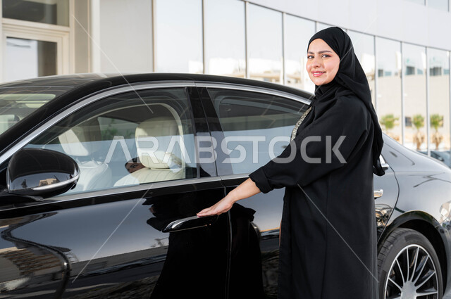 A woman's self-reliance in transportation and movement, readiness to ride a car, the concept of independence, freedom and self-reliance, a smiling Saudi Arabian Gulf woman wearing the hijab and abaya opening her car door, freedom to drive for the Arab woman