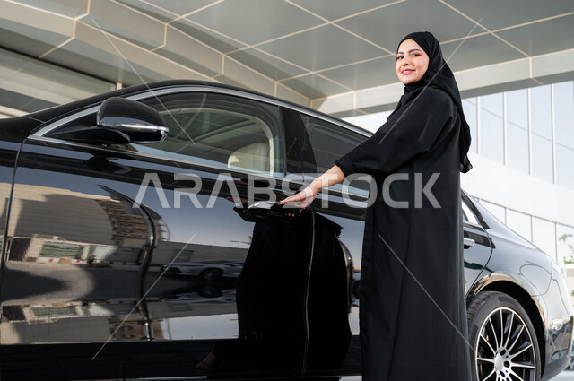 الاستعداد لركوب السياره، مفهوم الاستقلال والحرية والاعتماد على النفس، إمرأة عربية خليجية سعودية مبتمسة ترتدي الحجاب والعباءة تقوم بفتح باب سيارتها، حرية القيادة للسيدة العربية، اعتماد المرأه على نفسها في التنقل و المواصلات