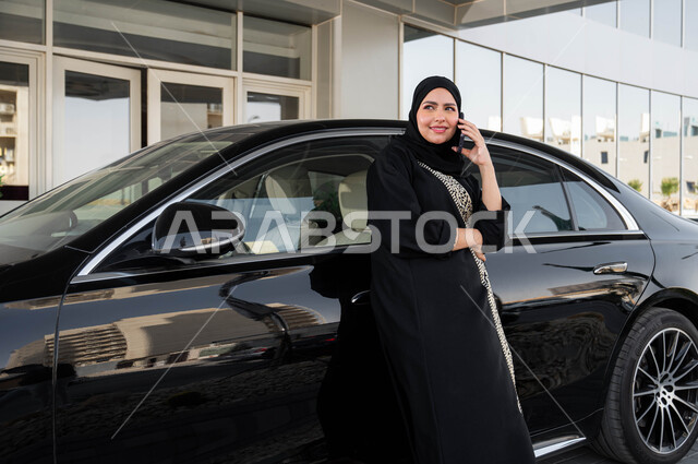 القيادة للذهاب الى العمل، استخدام الاجهزة التقنية الحديثة، سيده أعمال عربية خليجية سعودية ترتدي الحجاب والعباءة تستند على سيارتها تقوم بإجراء مكالمة هاتفية, مفهوم الاستقلال والحرية، اعتماد المرأه على نفسها في التنقل والمواصلات