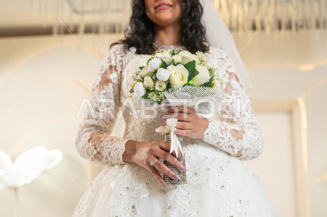باقات أزهار مميزة و فريدة، صورة مقربة لعروس عربية خليجية سعودية جميلة ترتدي فستان الزفاف الأبيض تمسك بيدها باقة ورد، الفرح و السرور في يوم الزواج، الاهتمام بالأناقة و المظهر الخارجي، مفهوم التزين والاطلالة المتألقة، قاعات الأفراح والمناسبات المزينة بالزهور