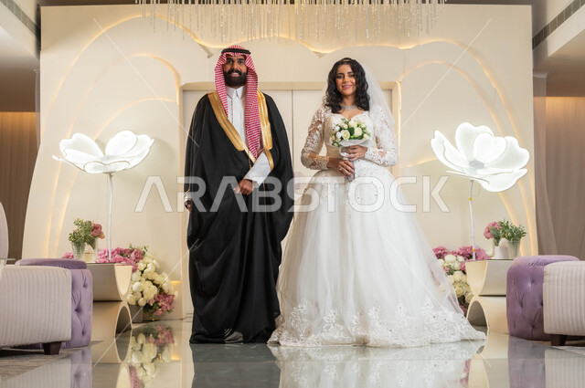 مراسم الاعراس و المناسبات في المملكة، الفرح و السرور في يوم الزفاف، اجمل إطلالة لرجل عربي وسيم يرتدي الزي الرسمي والبشت التقليدي، صورة لعروسة عربية خليجية سعودية ترتدي فستان زفاف أبيض تمسك بيدها باقة ورد، مفهوم الاستقرار وتكوين عائلة، أصالة العادات والتقاليد