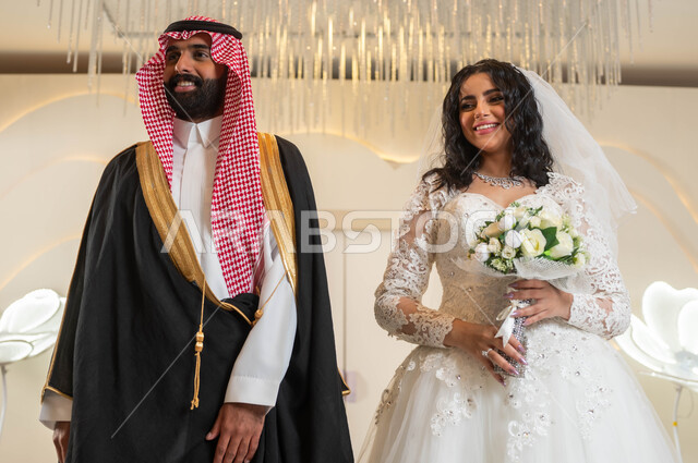 مفهوم الاستقرار وتكوين عائلة، اجمل إطلالة لرجل عربي وسيم يرتدي الزي الرسمي والبشت التقليدي، أصالة العادات والتقاليد، مراسم الاعراس و المناسبات في المملكة، الفرح و السرور في يوم الزفاف، صورة لعروسة عربية خليجية سعودية ترتدي فستان زفاف أبيض تمسك بيدها باقة ورد