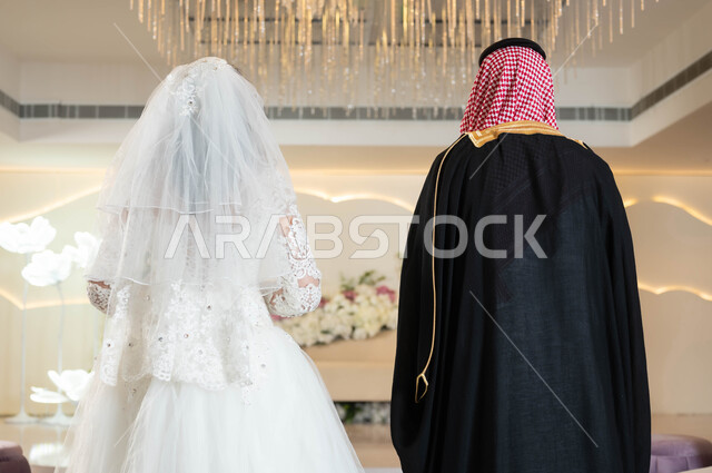 قاعات الأفراح المزينة بالورود و الزهور، عروس عربية جميلة تمسك بيدها باقة ورد، صورة من الخلف لعريس عربي خليجي سعودي، الاستقرار وتكوين عائلة، مفهوم الوفاء بالوعود، السرور والفرح في يوم الزواج، مراسم الأعراس والمناسبات في المملكة، الاهتمام بالمظهر الخارجي