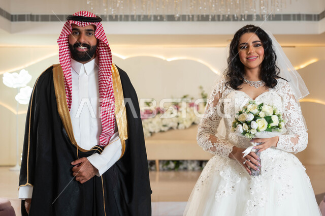 النظر إلى الكاميرابإيماءات السعادة، الأناقة والاهتمام بالمظهر الخارجي, صورة لعريس و عروس عربيان خليجيان سعوديان في قاعة الزفاف، المناسبات والأفراح الخاصة, مفهوم الاستقرار وتكوين الأسرة, السرور والفرح في يوم الزواج، مراسم الأعراس في المملكة