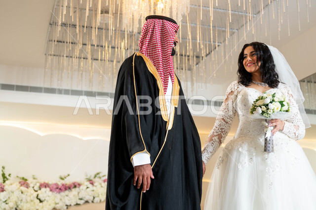 الاستقرار وتكوين عائلة، مفهوم الوفاء بالوعود، السرور والفرح في يوم الزواج، مراسم الأعراس والمناسبات في المملكة، صورة لعروس و عريس عربيان خليجيان سعوديان يمسكان الايدي ينظران لبعضهما بإيماءات الحب، قاعات الأفراح المزينة بالورود و الزهور