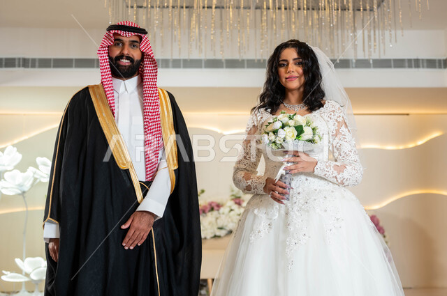 مراسم الاعراس و المناسبات في المملكة، الفرح و السرور في يوم الزواج، اجمل إطلالة لرجل عربي وسيم يرتدي الزي الرسمي والبشت التقليدي، صورة لعروسة عربية خليجية سعودية ترتدي فستان زفاف أبيض تمسك بيدها باقة ورد، مفهوم الاستقرار وتكوين عائلة، أصالة العادات والتقاليد
