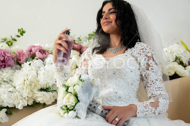 The concept of elegance and attention to external appearance, perfumes with luxurious and unique scents, a close-up photo of a Saudi Arabian Gulf bride wearing a white wedding dress carrying a perfume bottle applying perfume, celebration in the event and wedding hall, wedding ceremonies and celebrations in the Kingdom, joy and happiness on the day of marriage