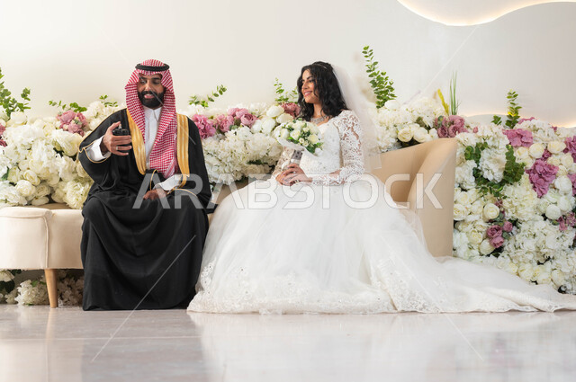 عطور فاخرة وفريدة، أصالة العادات والتقاليد،الفرح والسرور في يوم الزفاف، اجمل إطلالة لرجل عربي وسيم يرتدي الزي الرسمي والبشت التقليدي يقوم بوضع العطر، صورة لعروسة عربية خليجية سعودية ترتدي فستان زفاف أبيض تمسك بيدها باقة ورد، مراسم الاعراس والمناسبات في المملكة
