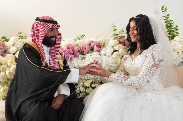 Exchanging wedding rings, wedding ceremonies and events in the Kingdom, joy and happiness on the wedding day, an Arab man wearing a formal dress and a traditional bisht, a close-up photo of a Saudi Arabian Gulf bride wearing a white dress, placing the ring at the wedding, wedding hall and events