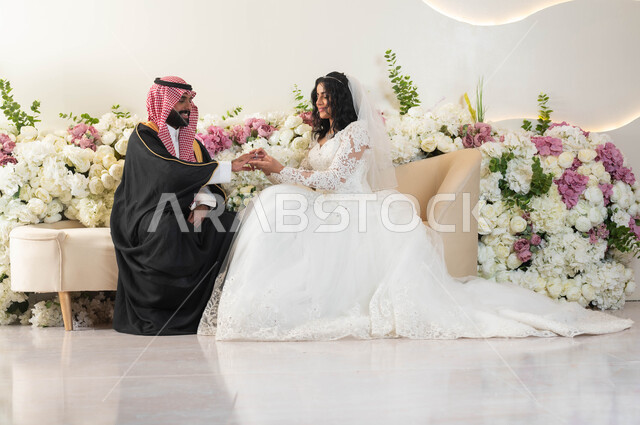 The concept of elegance and attention to the external appearance, joy and pleasure on the wedding day, replacing wedding rings, a picture of an Arab man wearing a formal uniform and a traditional bisht, the most beautiful look of a Saudi Arabian Gulf bride wearing a white dress, wedding and events hall, wedding ceremonies and events in the Kingdom