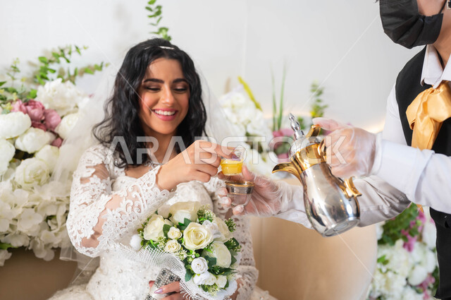 Celebration in the event and wedding hall decorated with flowers, a close-up of a hostess serving authentic Saudi coffee, a Saudi Arabian Gulf bride wearing a white wedding dress holding a bouquet of roses in her hand, taking a cup of hot drinks, wedding and marriage ceremonies