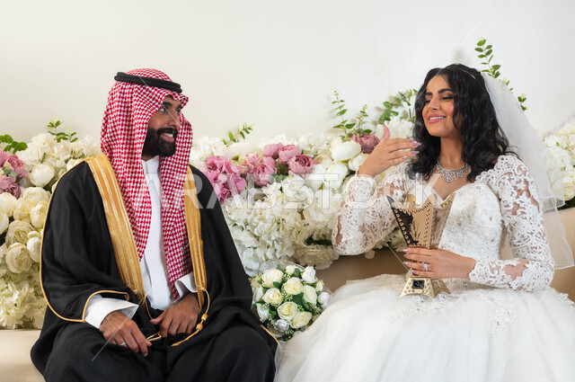 الفرح و السرور في يوم الزفاف، اجمل إطلالة لرجل عربي يرتدي الزي الرسمي والبشت التقليدي ينظر إلى عروسه بحب، صورة مقربة لعروسة عربية خليجية سعودية ترتدي فستان زفاف أبيض تمسك بيدها المبخرة، مراسم الاعراس و المناسبات في المملكة، مفهوم الاستقرار وتكوين عائلة