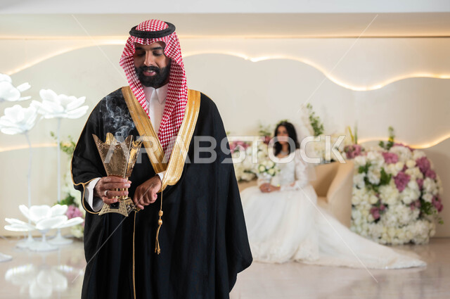 مفهوم الاستقرار وتكوين عائلة، اجمل إطلالة لرجل عربي يرتدي الزي الرسمي والبشت التقليدي يحمل المبخرة، صورة لعروسة عربية خليجية سعودية ترتدي فستان زفاف أبيض تمسك بيدها باقة الورود، مراسم الاعراس و المناسبات في المملكة، الفرح و السرور في يوم الزفاف