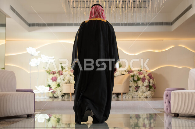 قاعات المناسبات والأفراح الفاخرة المزينة بالورود, الأناقة والاهتمام بالمظهر الخارجي، صورة من الخلف لعريس عربي سعودي خليجي يرتدي الزي الرسمي والبشت التقليدي يقف باستقامة, مراسم الأعراس والزواج في السعودية, صورة الجسم بالطول الكامل