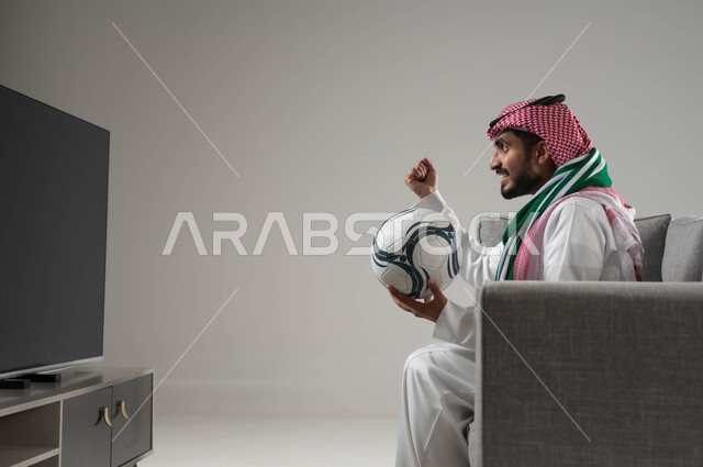المباريات والالعاب الرياضية, المنافسة والتحدي والتشجيع,  الشغف بمباريات كرة القدم, بوتريه لشاب عربي سعودي خليجي يرتدي الثوب التقليدي والشماغ يمسك بيده الكرة, ارتداء وشاح تشجيعي للفريق المفضل, رفع اليد بتعابير الفوز والانتصار, خلفية رمادية