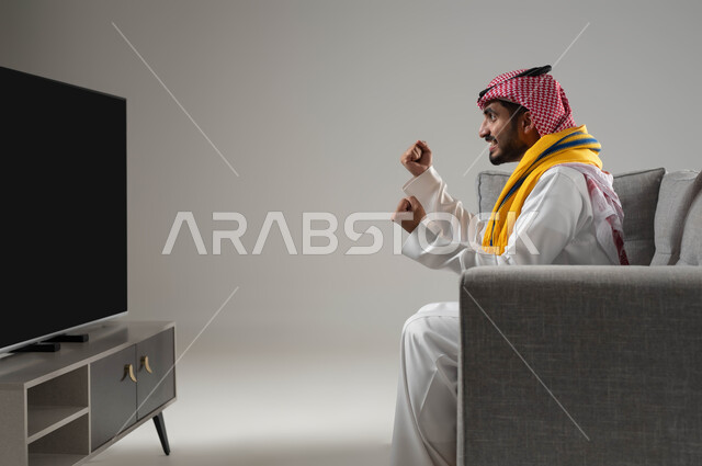 تعابير الحماس والفوز, الشغف بمباريات كرة الفدم, الانسجام والتفاعل مع المنافسة, رفع اليدين الى الاعلى بتعابير الانتصار, بورتريه لشاب عربي سعودي خليجي يرتدي الثوب التقليدي والشماغ, ارتداء وشاح التشجيع, خلفية رمادية