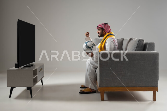 الانسجام والتفاعل مع المنافسة, الشغف بمباريات كرة الفدم, رفع اليد الى الاعلى بتعابير الفوز والانتصار, بورتريه لشاب عربي سعودي خليجي يرتدي الثوب التقليدي والشماغ يمسك الكرة, ارتداء وشاح التشجيع, خلفية رمادية