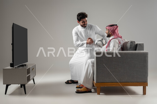 التفاعل والاندماج بمشاهدة الفريق المفضل, المباريات والالعاب الرياضية, ايماءات الفرح والحماس بالفوز والانتصار, بورتريه لرجلان عربيان سعوديان خليجيان احدهما يمسك بيده كرة قدم, الشغف بالانشطة الترفيهية, خلفية رمادية