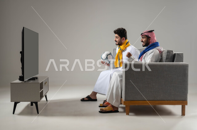 Cheerfulness and integration to achieve victory and triumph, passion for pursuing sports activities, expressions of enthusiasm and excitement, spending fun and entertaining times with friends, portrait of two Saudi Gulf Arab men wearing scarves for the Crimean football teams, gray background