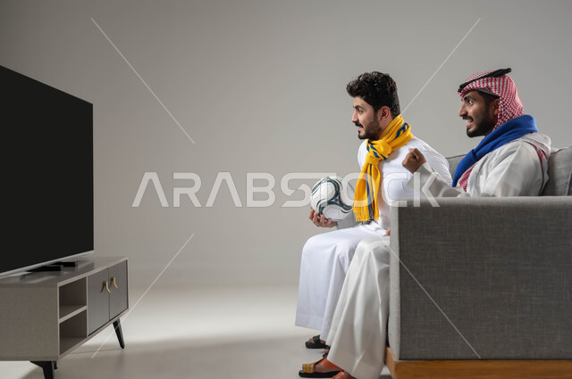 الشغف بمتابعة الانشطة الرياضية, تعابير الحماس والتشويق, قضاء اوقات ممتعة ومسلية مع الاصدقاء, البشاشة والاندماج لتحقيق الفوز والانتصار, بورتريه لرجلان عربيان سعوديان خليجيان يرتديان اوشحة تشجيعية لفرق كرة القرم, خلفية رمادية