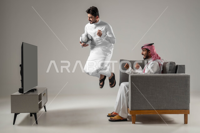 الانتصار و تحقيق الأهداف، بورتريه لرجلان عربيان سعوديان يحتفلان بفوز فريقهم المفضل، القفزعالياً بحماس، ايماءات الفرح والسعادة والسرور، قضاء وقت الفراغ بمشاهدة التلفاز مع الأصدقاء، متابعة مباراة كرة القدم، خلفية رمادية